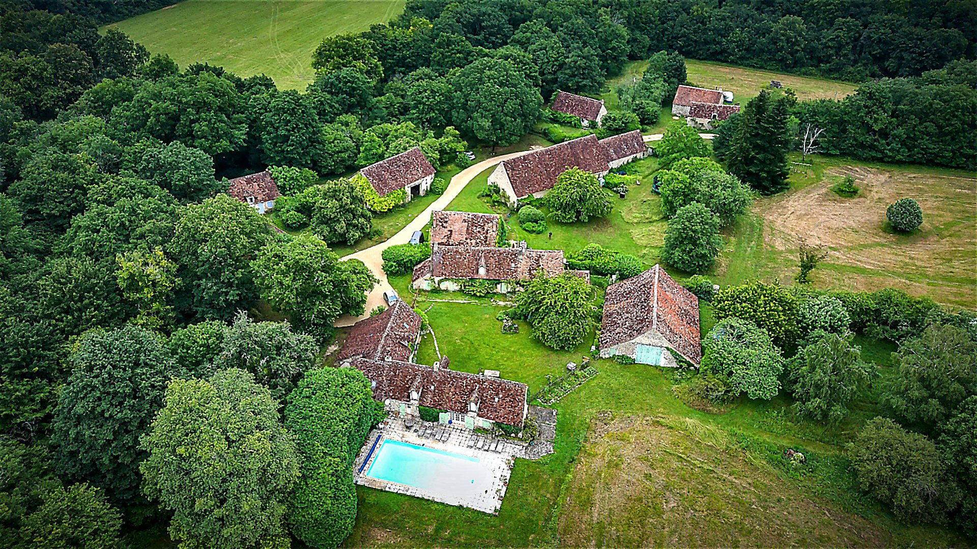 Vue aérienne du Hameau des Rabauds : maisons de pierre aux toits de tuiles anciennes, piscine et bois de chênes, hameau du XVIIe siècle dans la Vienne
